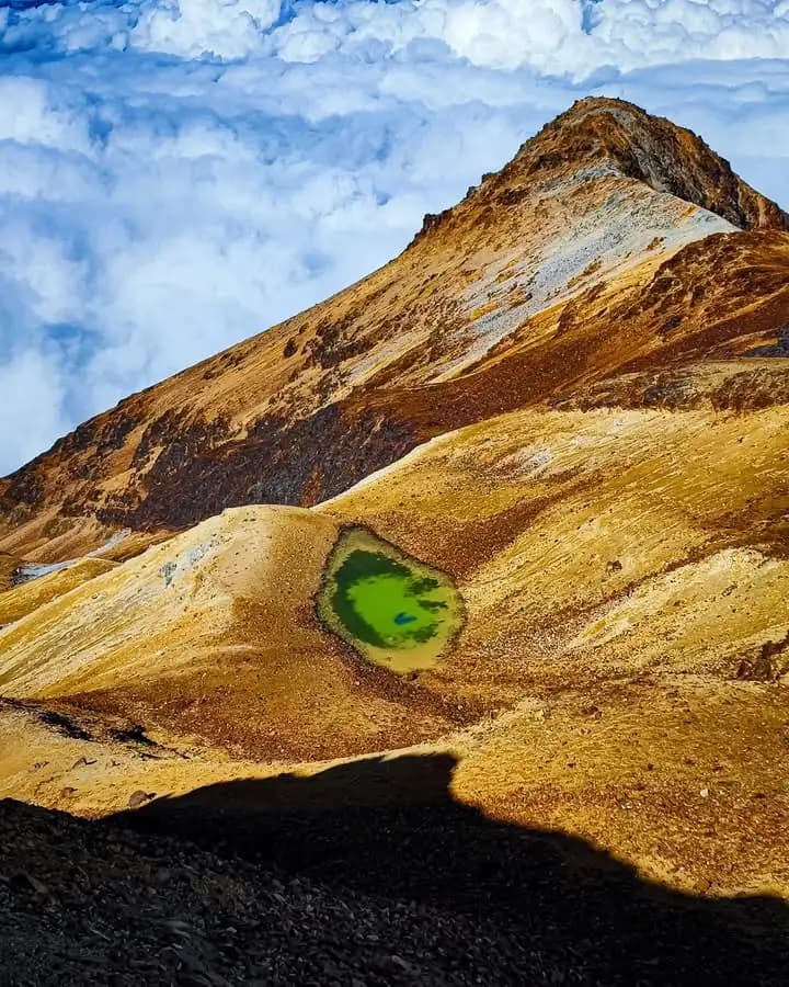 Pequeña laguna verde en una depresión entre colinas doradas del páramo.