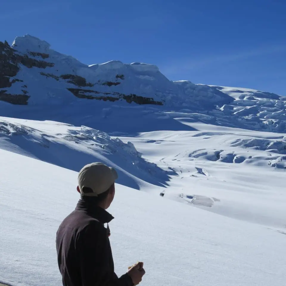 Persona observando una planicie de nieve y glaciar bajo cielo despejado.