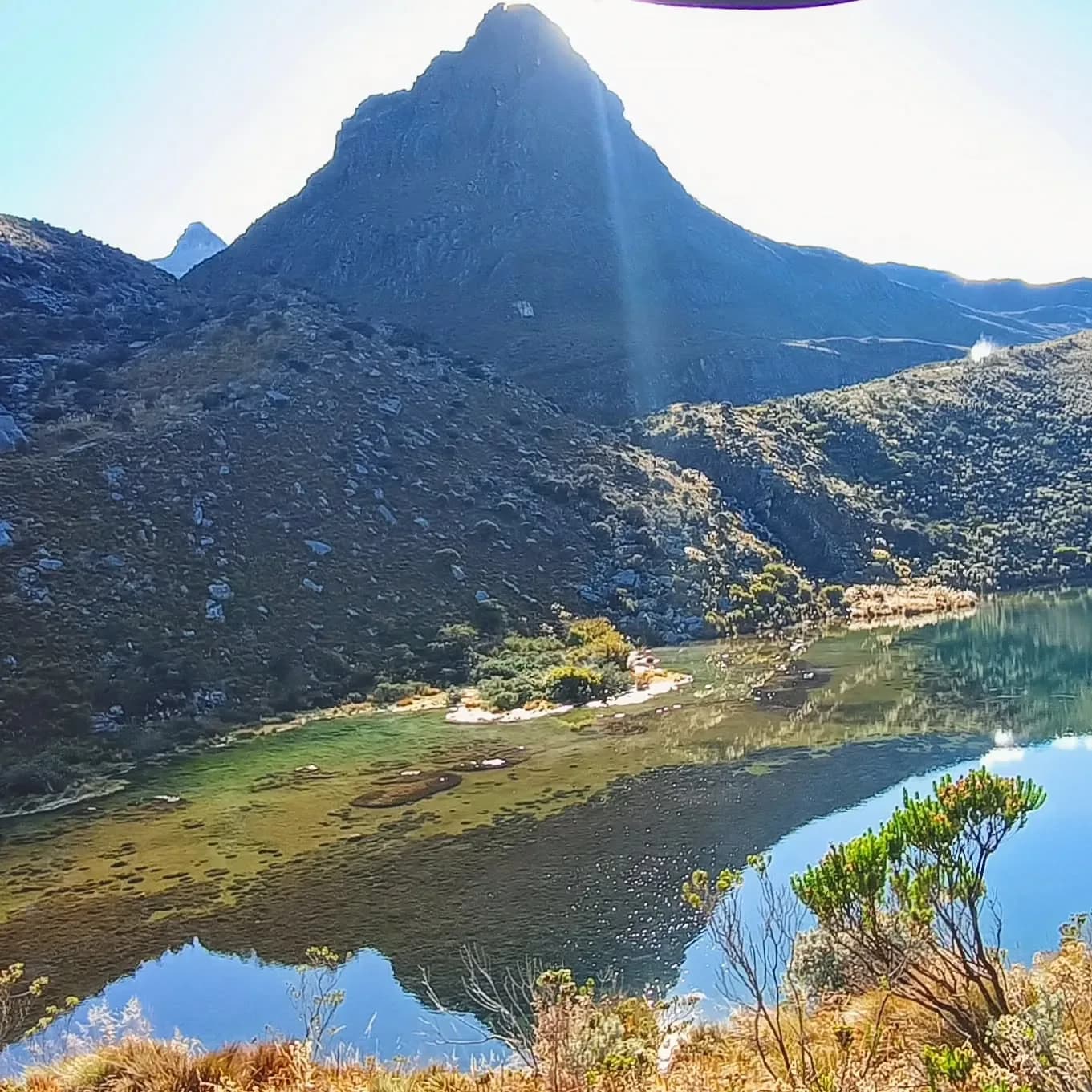 Laguna rodeada de montañas verdes bajo la luz del sol.